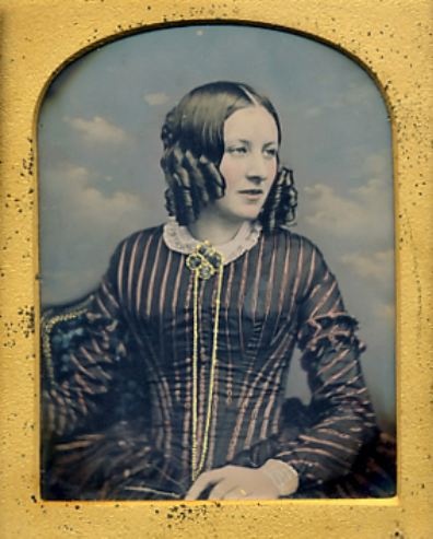 ca 1850’s hand-tinted daguerreotype portrait of a young woman posed in front of a cloud backdrop