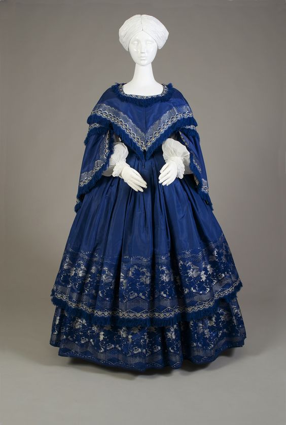 Blue silk taffeta evening dress with two-tier skirt. All hems are finished with a border of silver floral jacquard ribbon and fringe. American, ca. 1855 Silk taffeta, jacquard woven ribbon, silk fringe, KSUM 2005.6.4 a-d