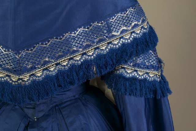 Blue silk taffeta evening dress with two-tier skirt. All hems are finished with a border of silver floral jacquard ribbon and fringe. American, ca. 1855 Silk taffeta, jacquard woven ribbon, silk fringe, KSUM 2005.6.4 a-d