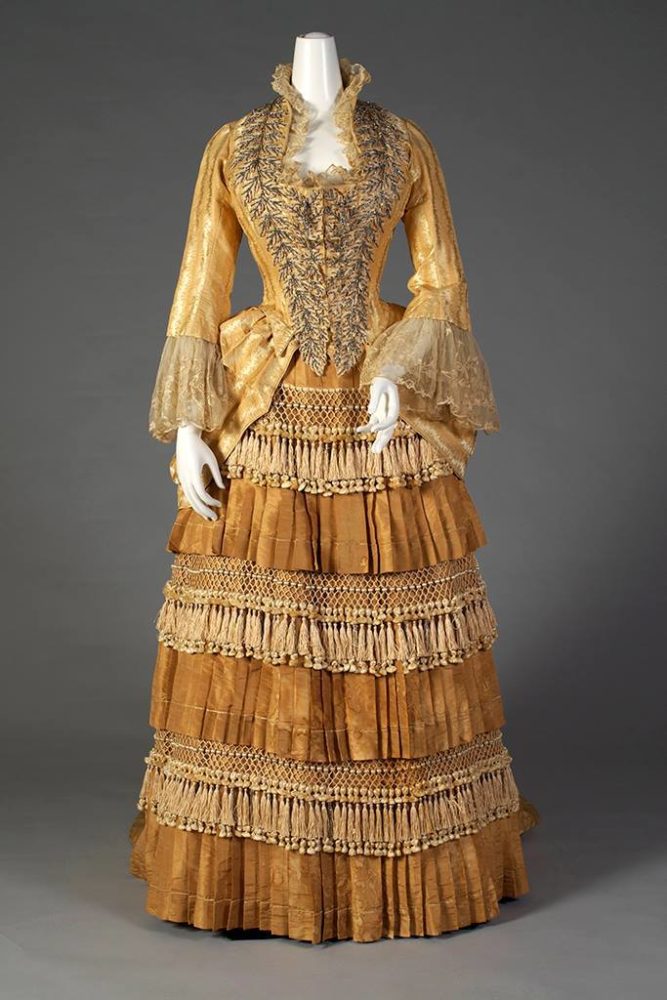 Gold silk dress with tiered, tasseled skirt Label- “Mrs. W. Wilds, Auburn, NY” American, ca. 1879-80, SIlverman:Rodgers, Kent State University Museum 1983.1.156 ab