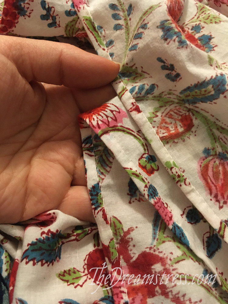 A hand holding a length of floral fabric with a hand-sewn hem