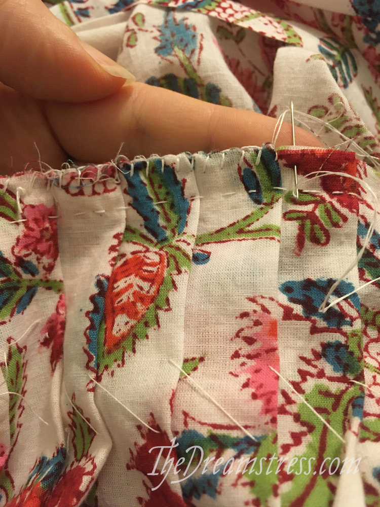 A hand holding a length of floral fabric with the raw hem edge finished with blanket stitches