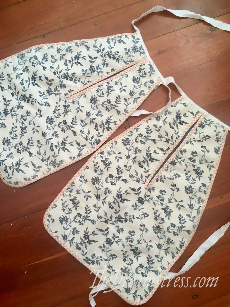 A pair of hanging 18th century womens pockets made of blue and white floral fabric, with red and white floral binding, lay on a wooden floor.