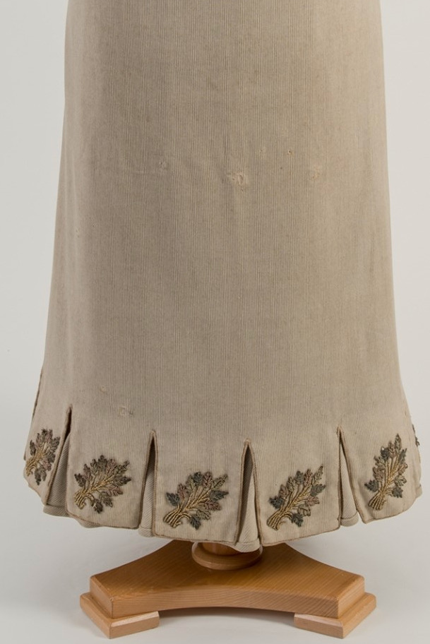 Image shows the hem of a light grey-beige skirt, with slit tabs and leaf embroidery