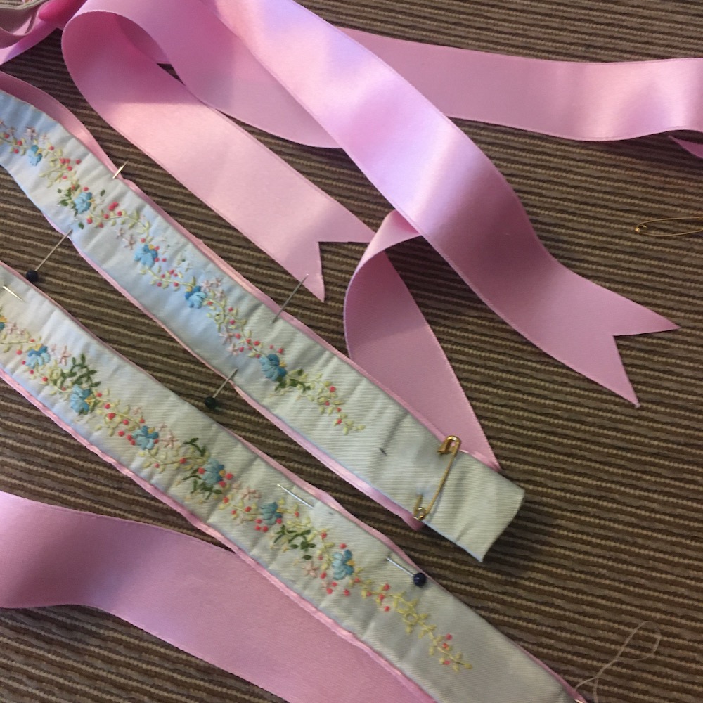 Image shows blue garters embroidered with little flowers sewn to pink silk ribbon 