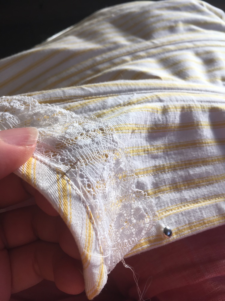 Image shows a hand holding a yellow and white striped corset, with a length of lace being sewn to it