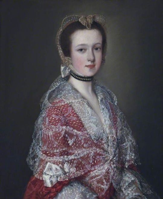 An 18th century painting showing a lady with dark hair in 3/4 view, wearing a pink-red dress with a sheer lace mantle over it.