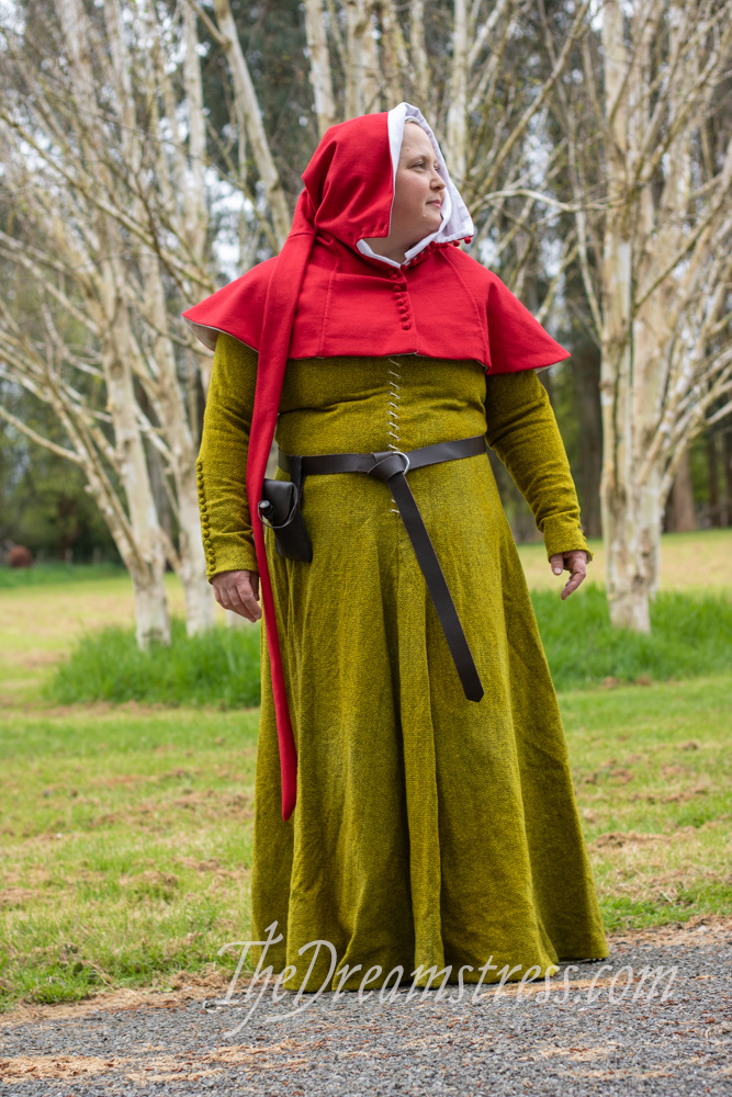 A woman wears a yellow-green kirtle and red hood lined with white. She looks to the right.