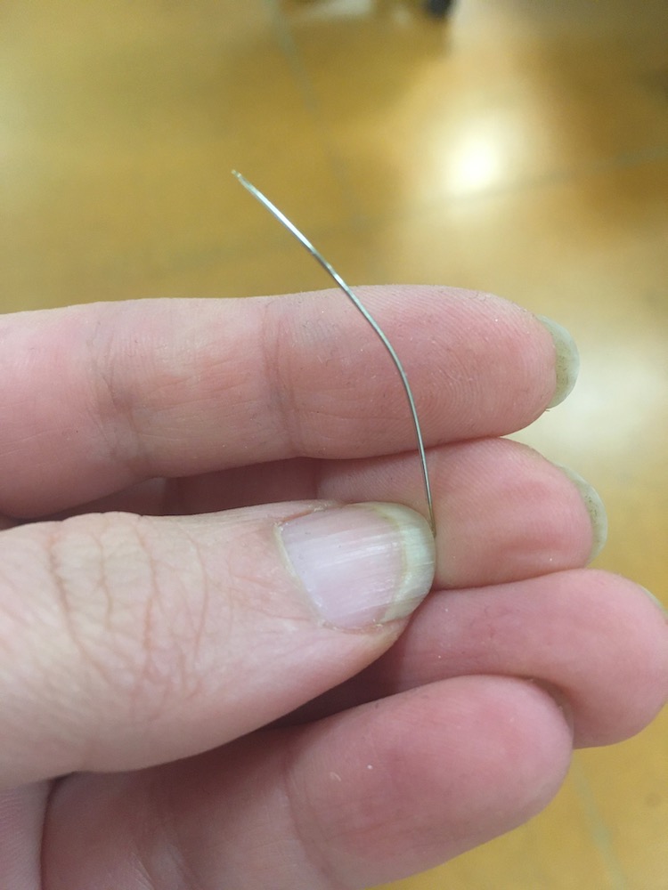 Photo shows a hand holding a bent needle